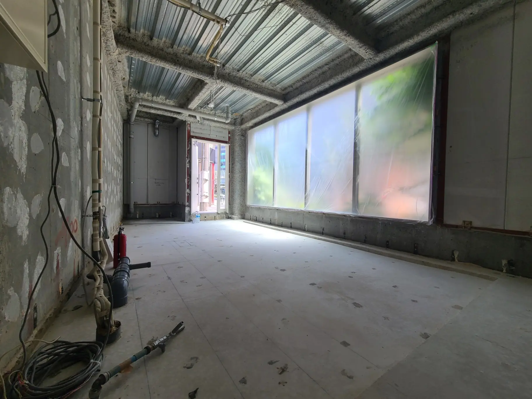 工事中の建物内部、露出した配管と電線、自然光が差し込む大窓、改装前のインテリア