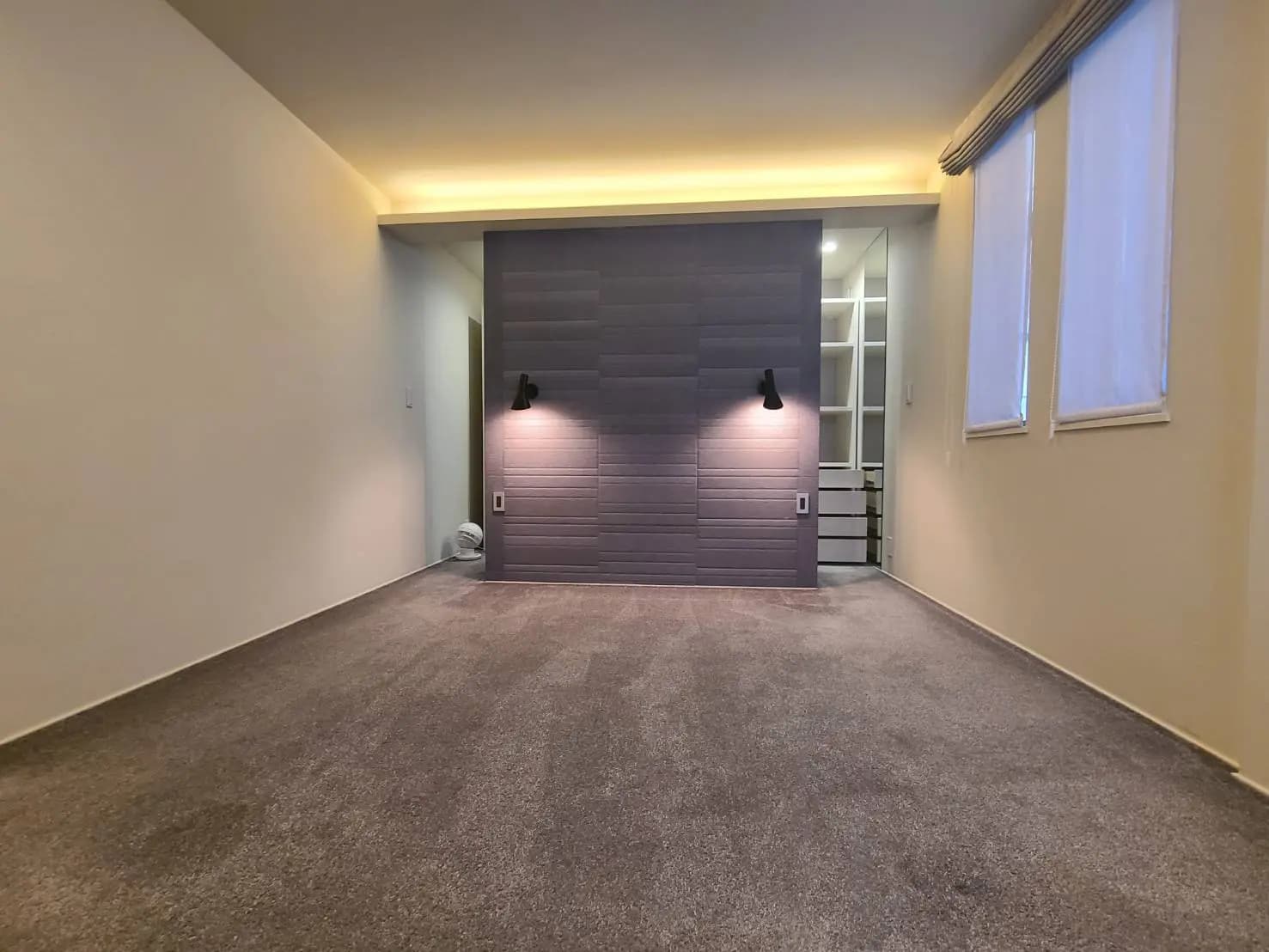 シンプルなデザインの空の部屋、グレーのカーペット、壁に組み込まれた照明と棚、小さな窓からの自然光