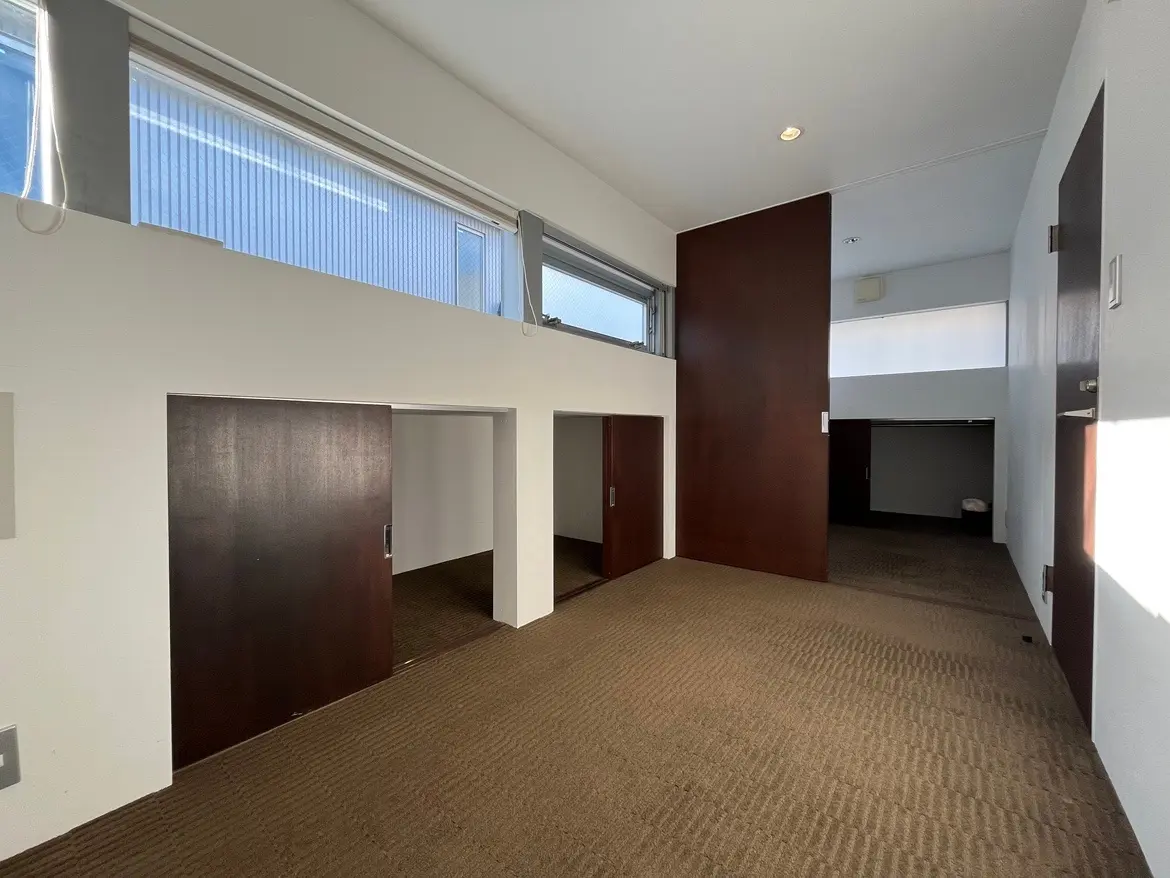 - モダンなデザインの部屋、背の高い窓から自然光が差し込み、木製の扉とカーペットが施された空間
