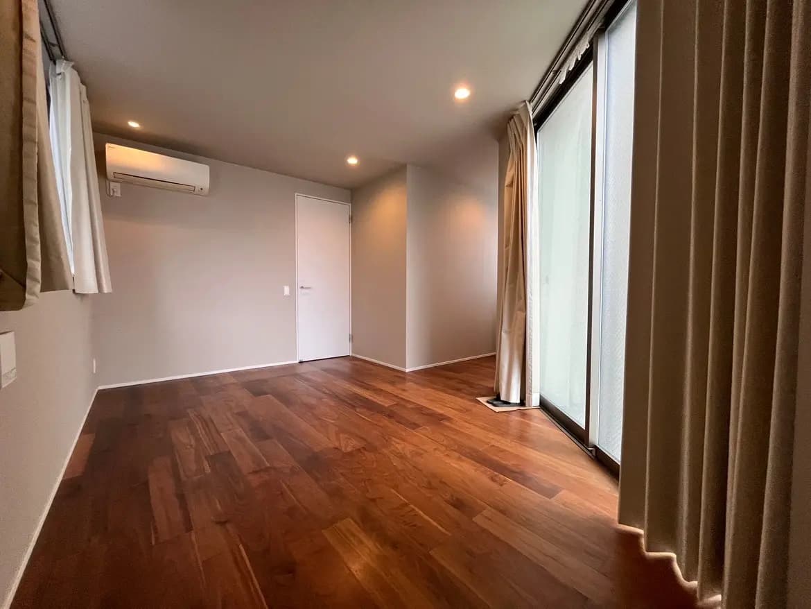 - 明るい色調のシンプルな部屋、木製フローリング、大きな窓からの自然光とエアコンが備わったインテリア