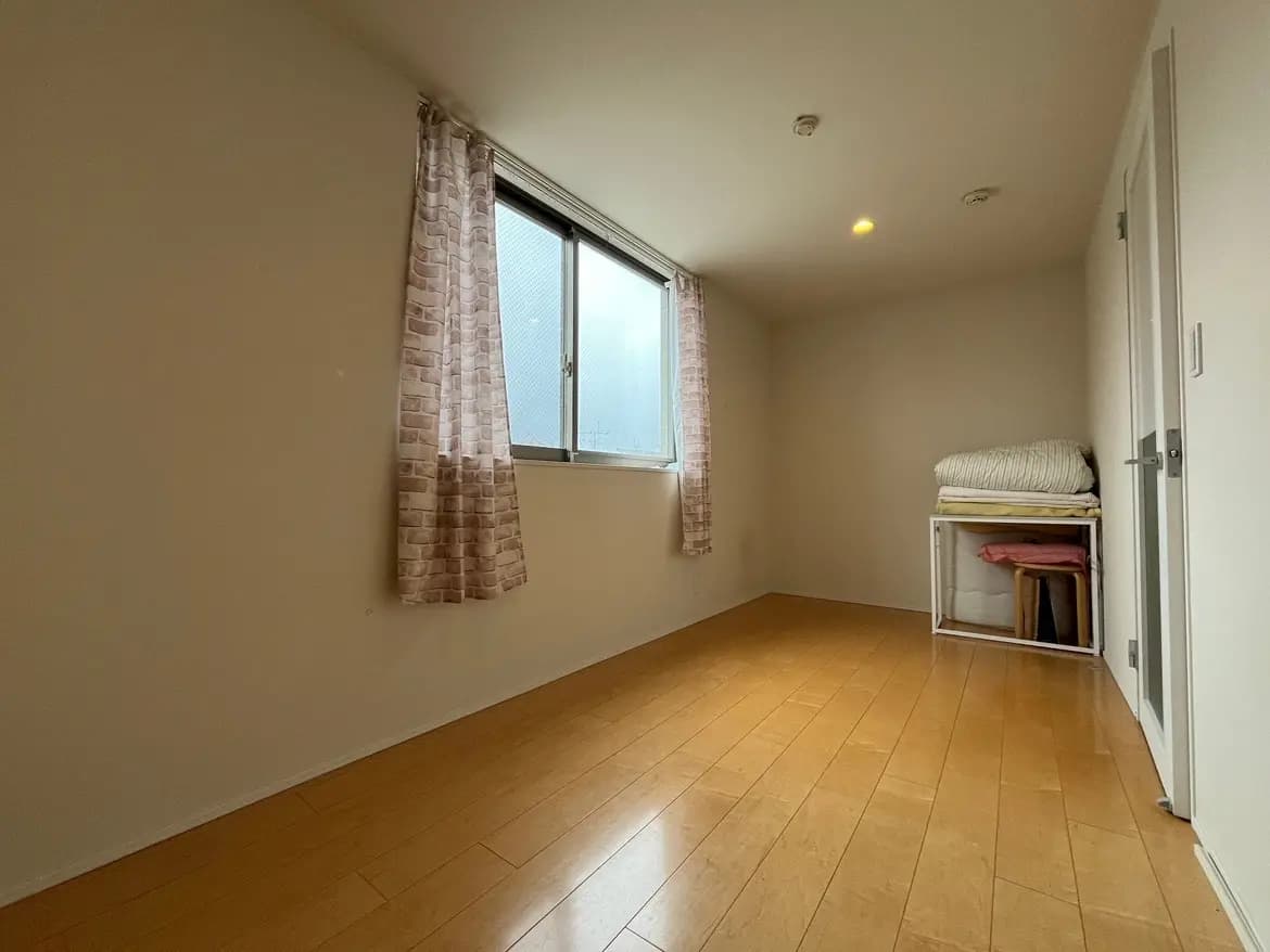 - 自然光が差し込むシンプルな部屋、木製フローリングと窓のカーテン、整理された収納スペースのインテリア