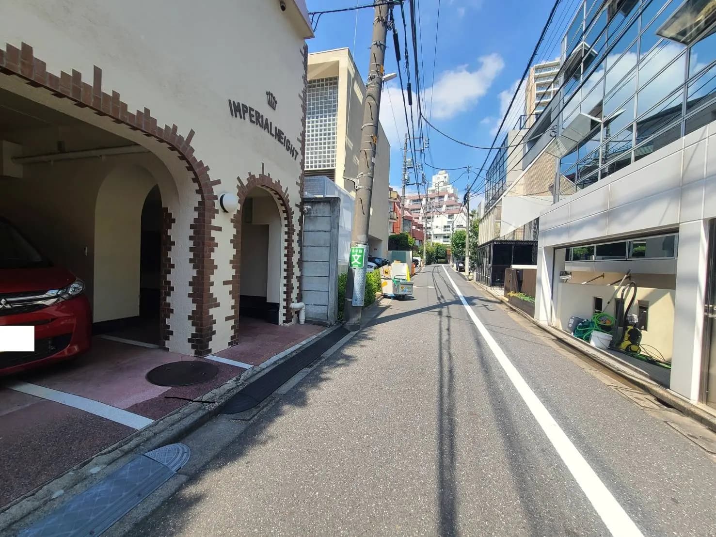 - 住宅街の通りに面した駐車場、アーチ型の入口と赤い車、周囲に立ち並ぶビルの風景