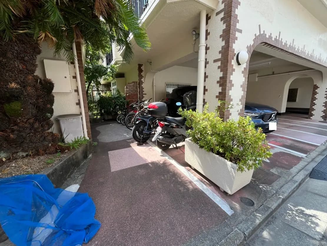 - 駐車場に並ぶ自転車とバイク、緑の植物が配置されたエントランス周辺の光景