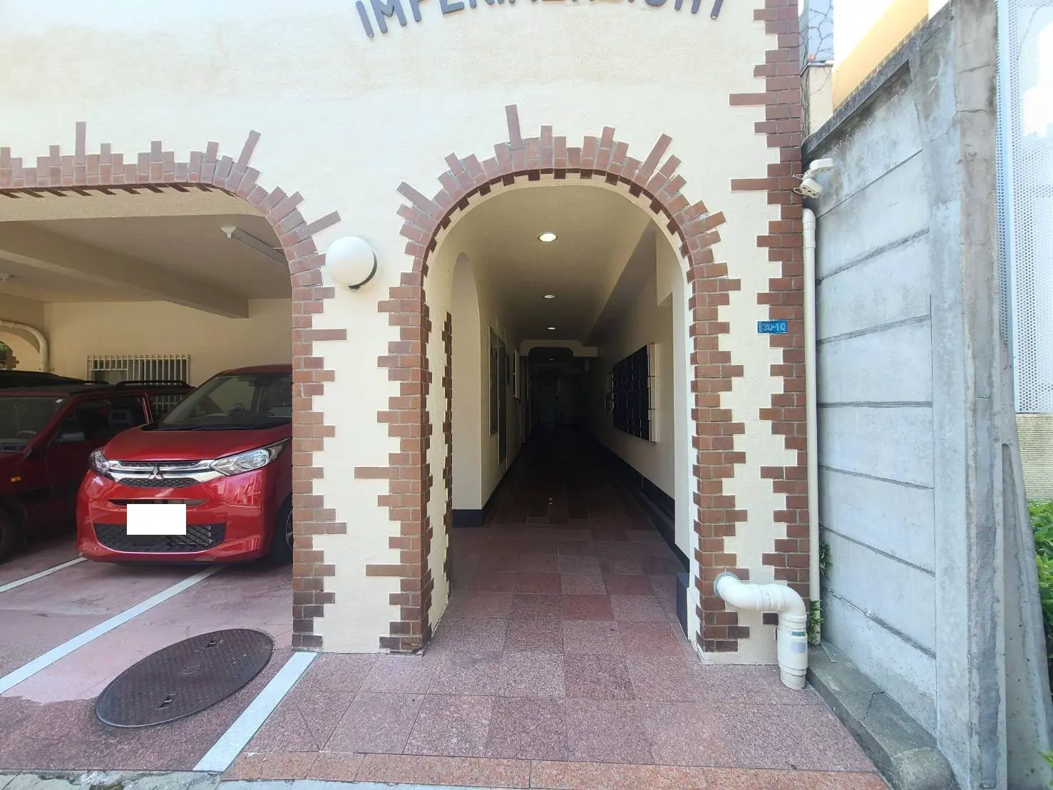 - 赤い車が停車するアーケードの入口、レンガ調の装飾が施された壁、奥に続く長い廊下の風景