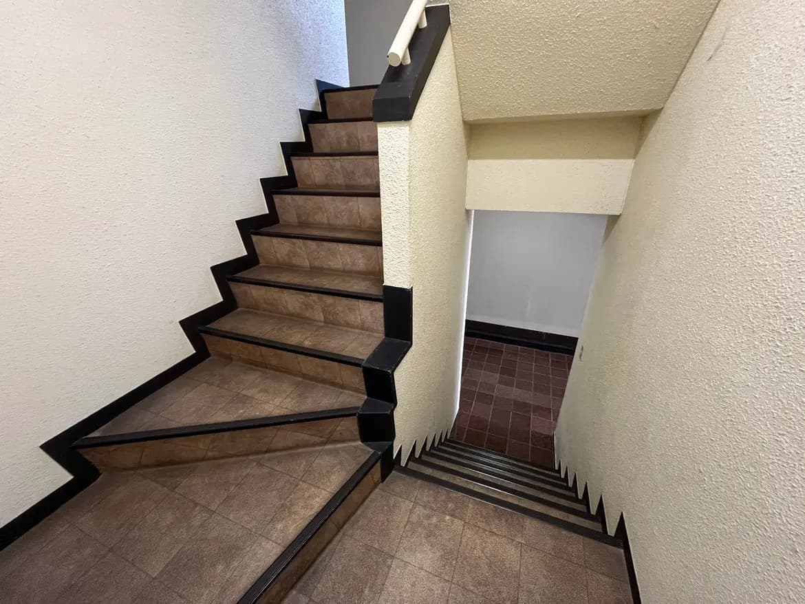 - 明るい照明に照らされた階段、茶色いタイルのステップと黒い手すりが特徴的な内部の景観