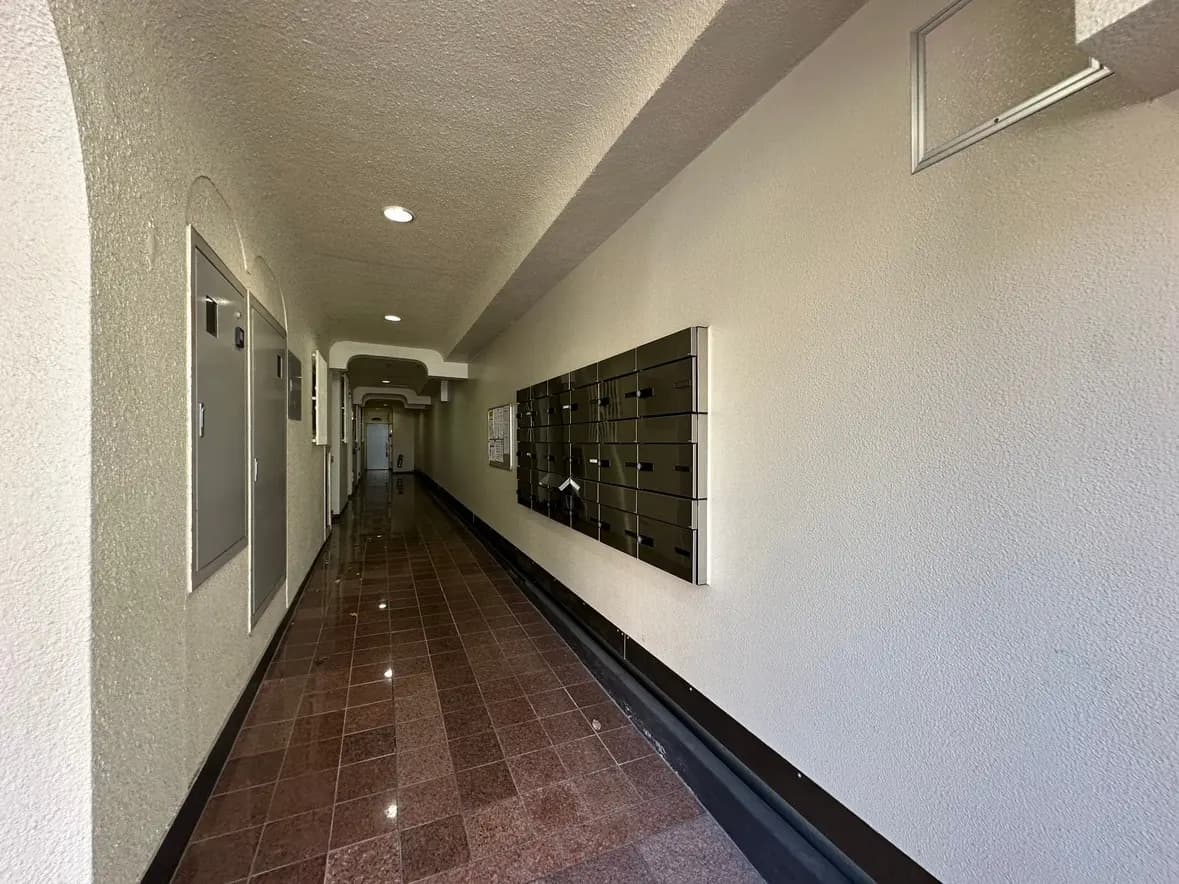 アパートの廊下、照明が設置された天井と光沢のある赤茶色のタイル床、壁に取り付けられた郵便受け