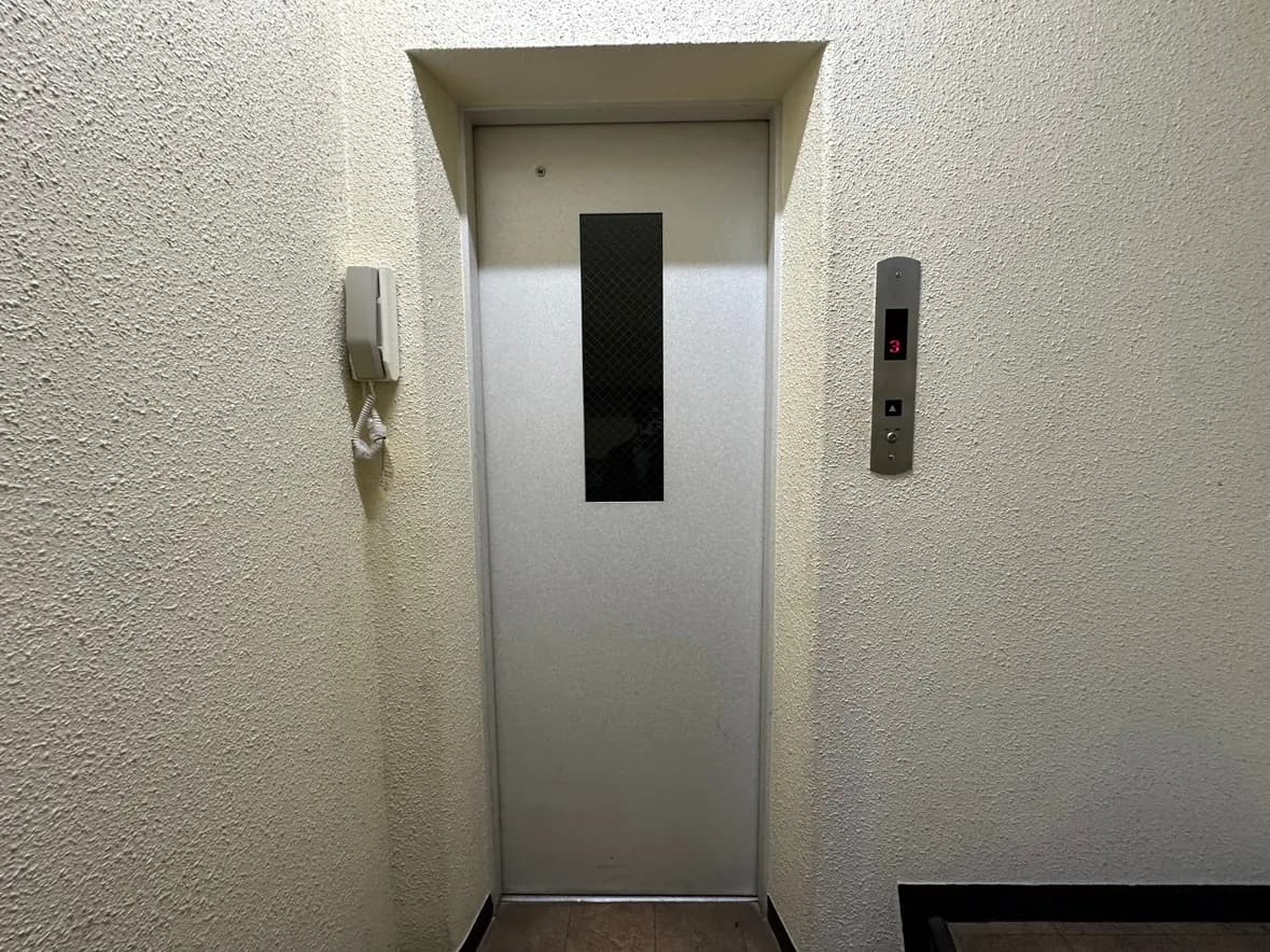 ビル内のエレベーター入口、非常通報装置と階数表示パネルがある廊下