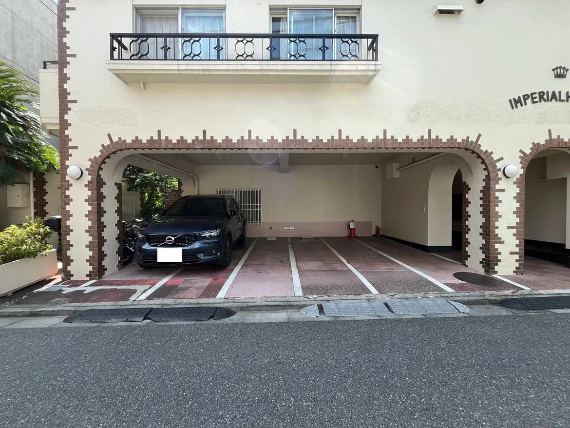 - アーチ型のガレージに停められた黒いボルボSUV、周囲には植栽とアーケードスタイルの建物が見える駐車スペース