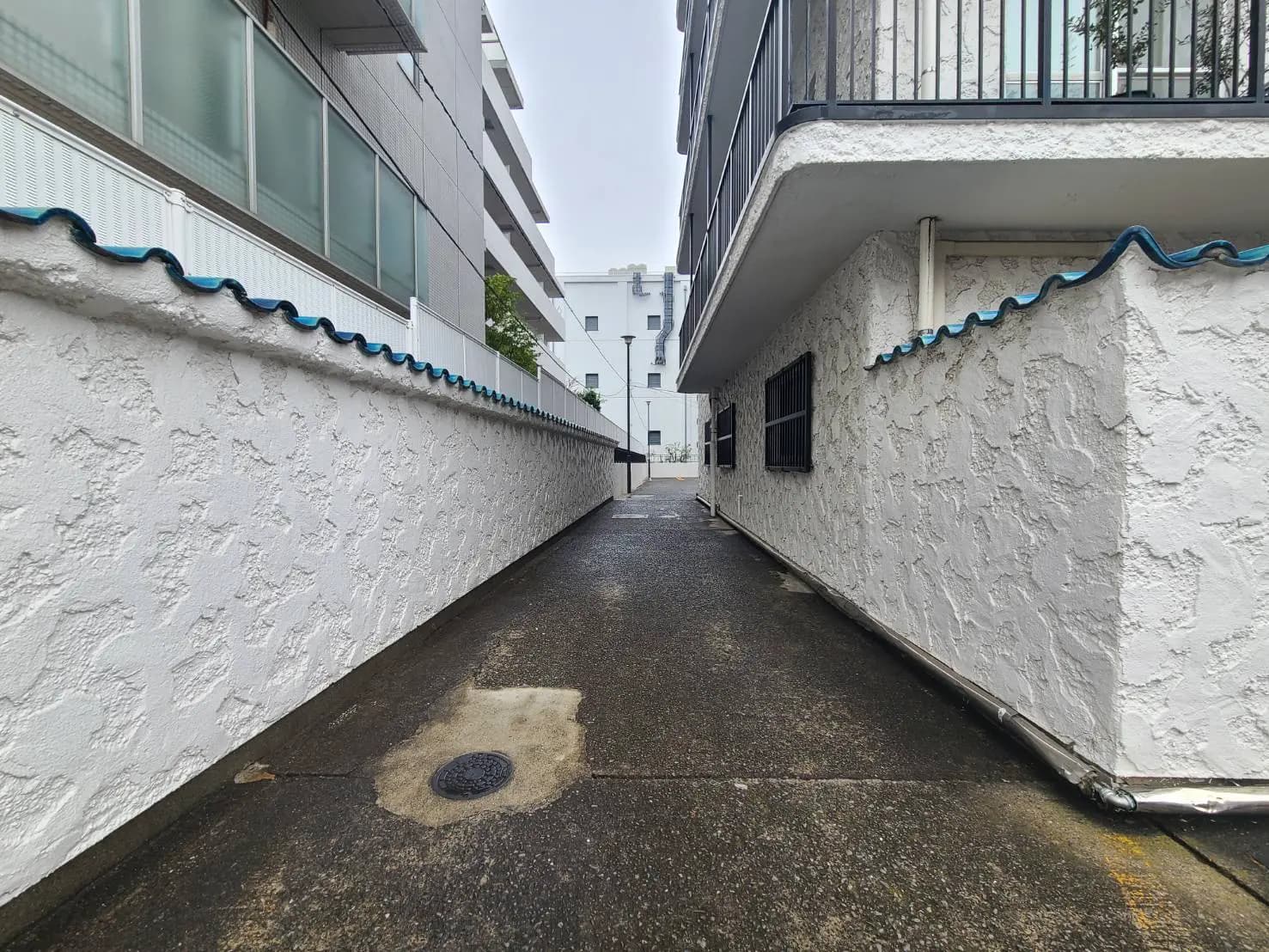 狭い都市の路地、白い壁と青い装飾の建物、濡れたアスファルト