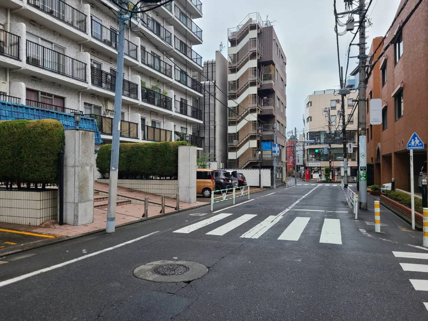 日本の都市風景、歩道と横断歩道、周囲にアパートと商業ビル、くもりの空