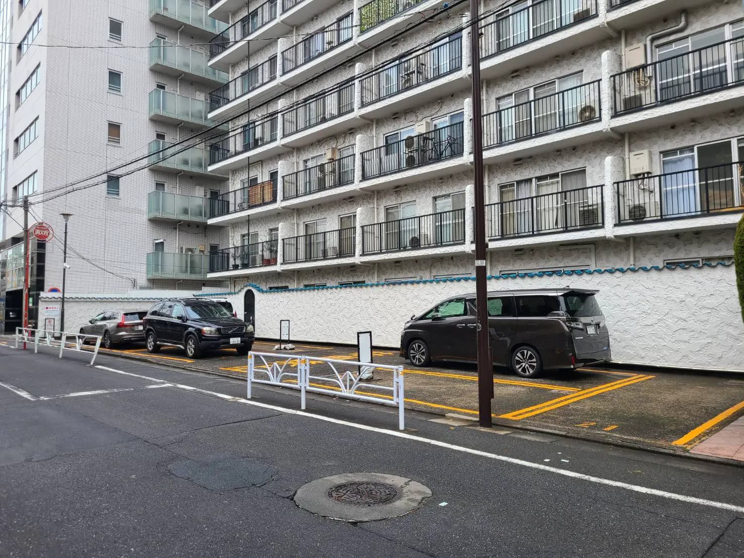 都市のマンションと駐車スペース、路上駐車あり、普通車数台と住宅街の風景