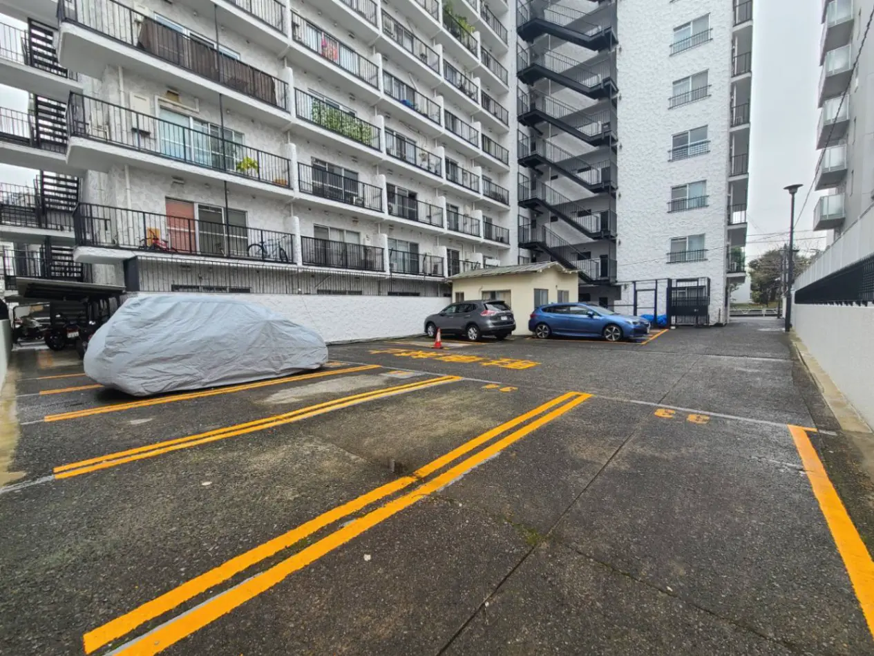 都市のマンション駐車場、車カバーがかけられた車と黄色の駐車スペースライン