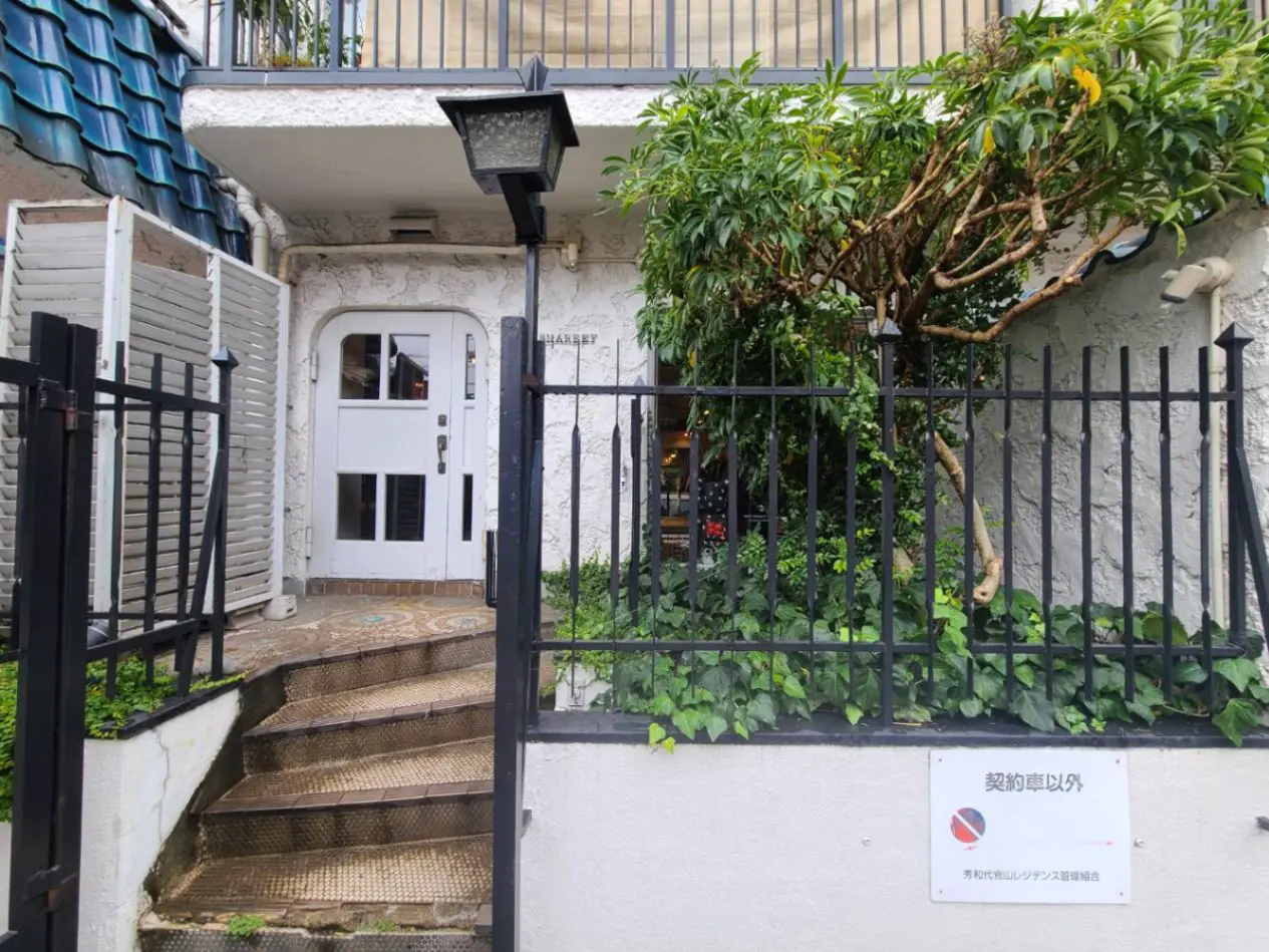 閑静な住宅地にあるユニークなデザインの白い家の入口とゲート、植栽に囲まれた階段と外灯