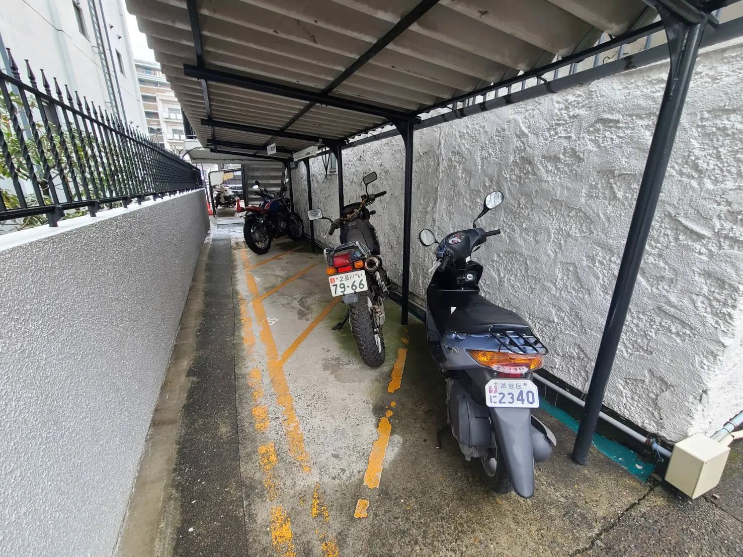 屋根付きのバイク駐輪場、コンクリートの壁、駐輪スペースに停まる複数のバイク