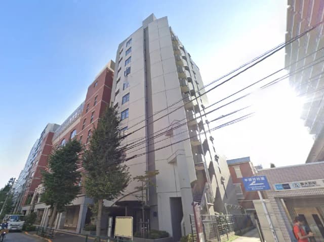 - 都市型マンションの外観、近隣に樹木や電柱があり、晴れた青空が広がる風景