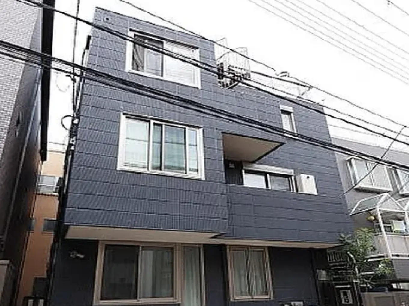 - モダンなデザインの三階建てのアパートメント、グレーの外壁と大きな窓、隣接する建物との距離感が特徴的な景観