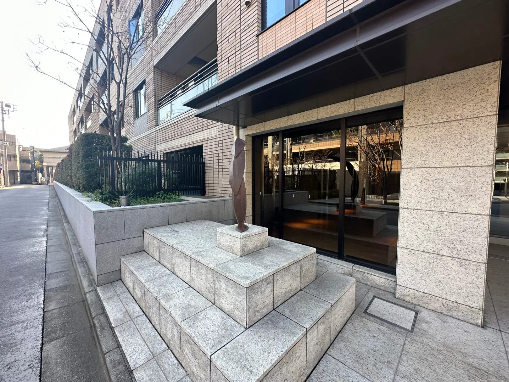 モダンな建物のエントランス、石造りの階段と彫刻、ガラス扉と反射する窓