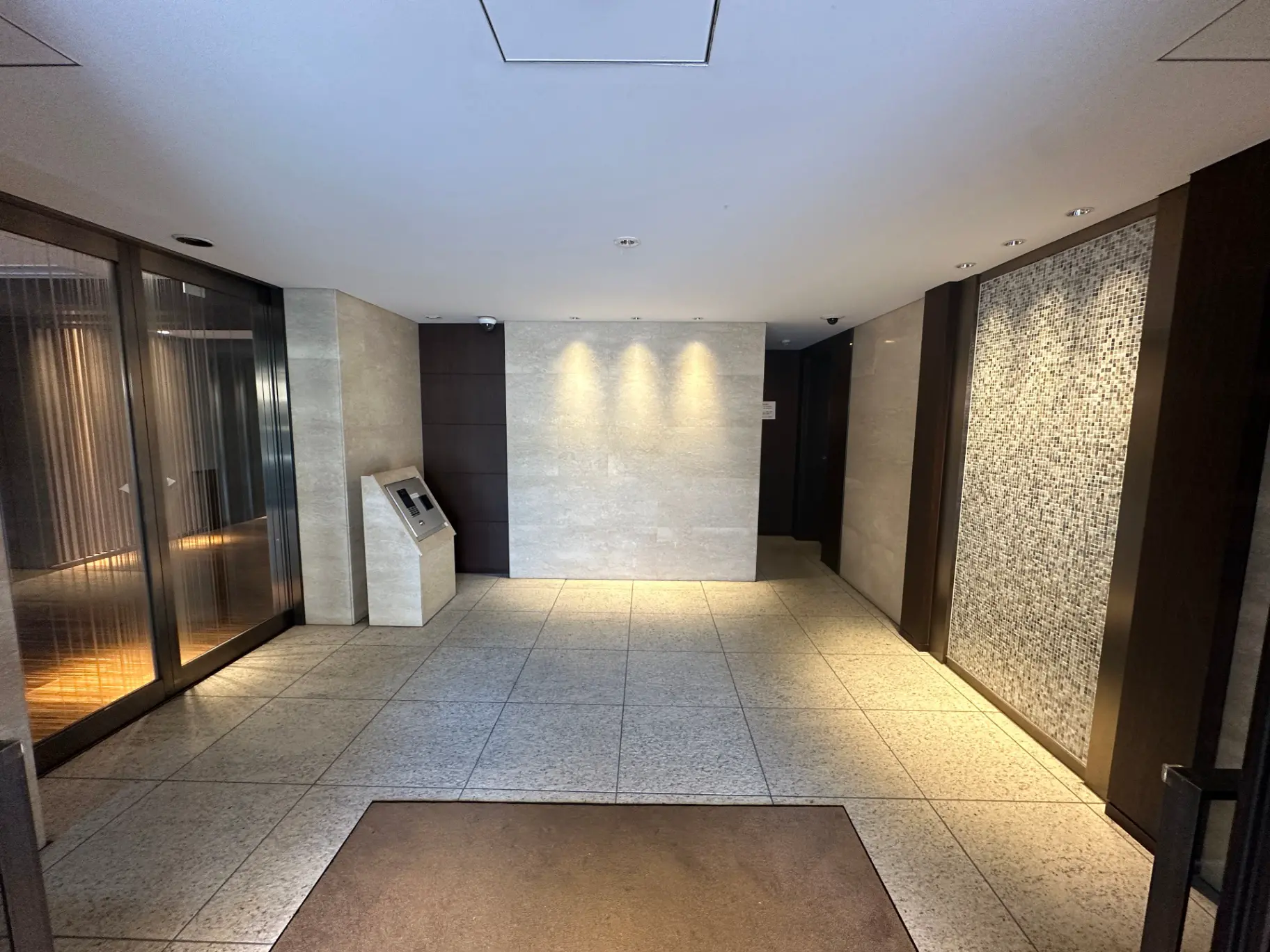現代的なデザインのエントランスホール、天井照明、タイル床、エレベーターとインターホンシステム