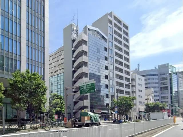 日差しが降り注ぐ市街地の景観、現代的なオフィスビルと道路沿いの緑豊かな樹木