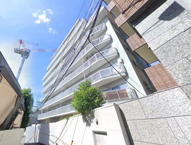 都市の住宅地に位置する現代的なマンションの外観、晴れた日のクレーンが見える建築現場