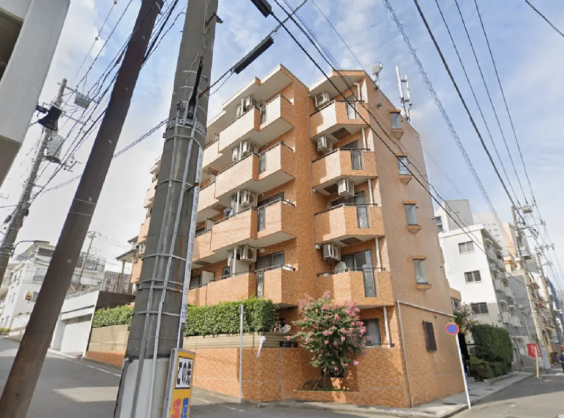 - モダンな外観のアパートメントビル、複数のバルコニーとエアコンが設置され、周囲は道路と電柱に囲まれた景観