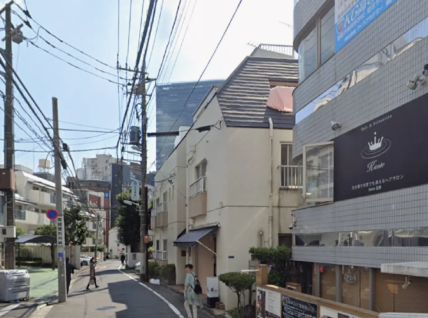 - 商業ビルと白い住宅が並ぶ街並み、道路沿いの電柱と電線が見える風景