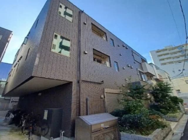 - モダンな外観のアパート、レンガ調の壁、緑豊かな庭と自転車置き場、青空を背景にした住宅街の一角