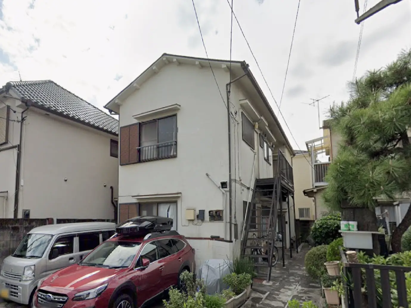 - 住宅の外観、茶色の窓が特徴的で、駐車場には赤いSUVと軽自動車が停まっている風景、近くに緑の植木がある場所