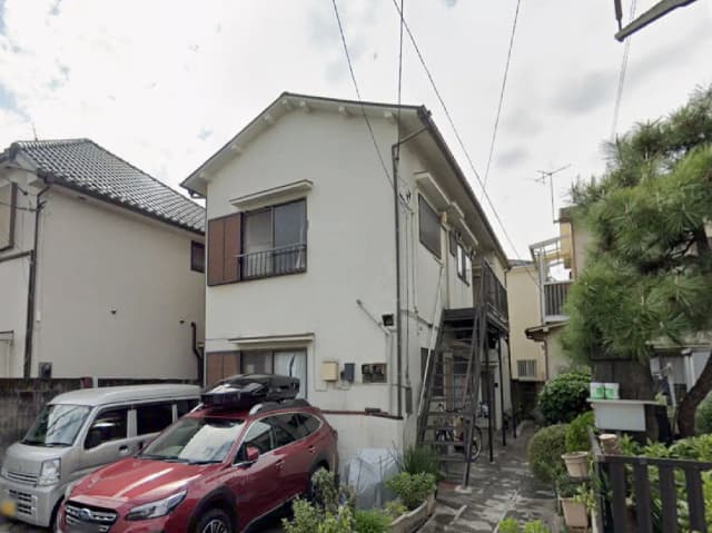 - 住宅の外観、茶色の窓が特徴的で、駐車場には赤いSUVと軽自動車が停まっている風景、近くに緑の植木がある場所