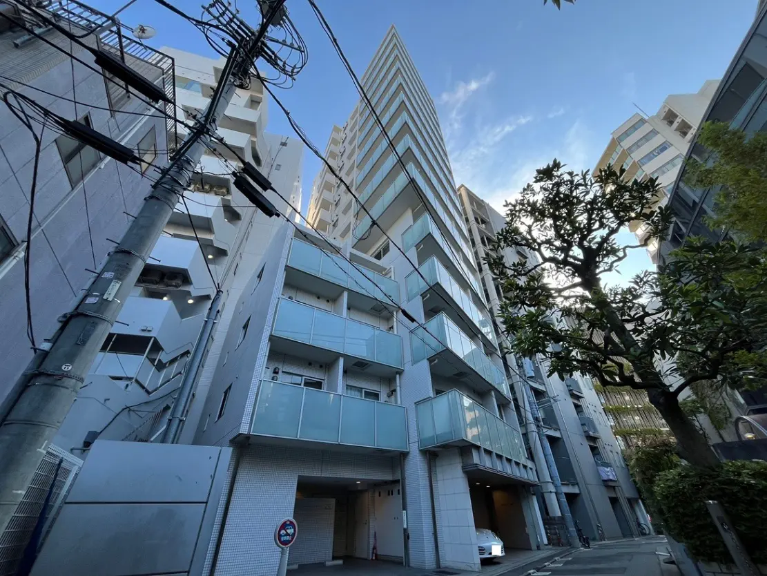 - 都市の高層ビルが立ち並ぶ風景、電柱と電線が交錯し、青空の下に佇むマンションの外観