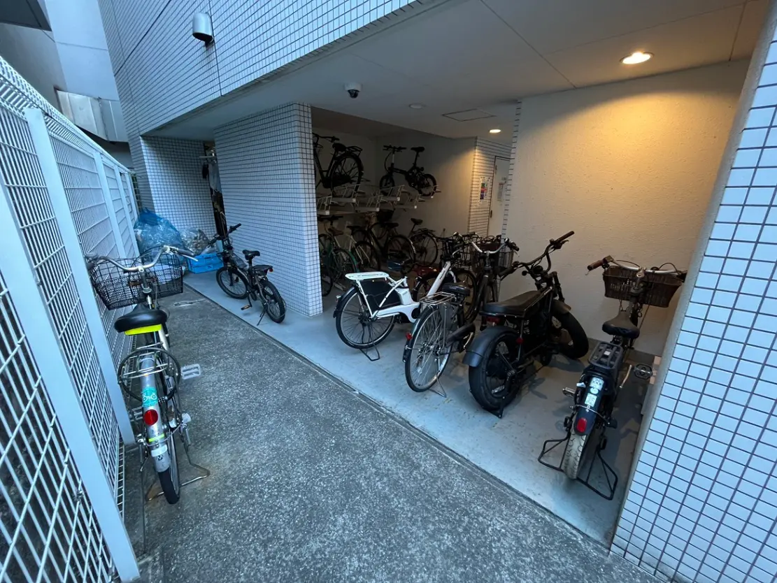- 自転車が並ぶ駐輪スペース、白いタイルの壁と照明がある屋根付きのエリア、整然とした配置の自転車たち