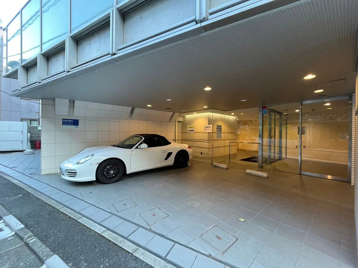 白いスポーツカーが駐車された現代的なエントランス、ガラスのファサードと広々としたテラスが特徴の建物