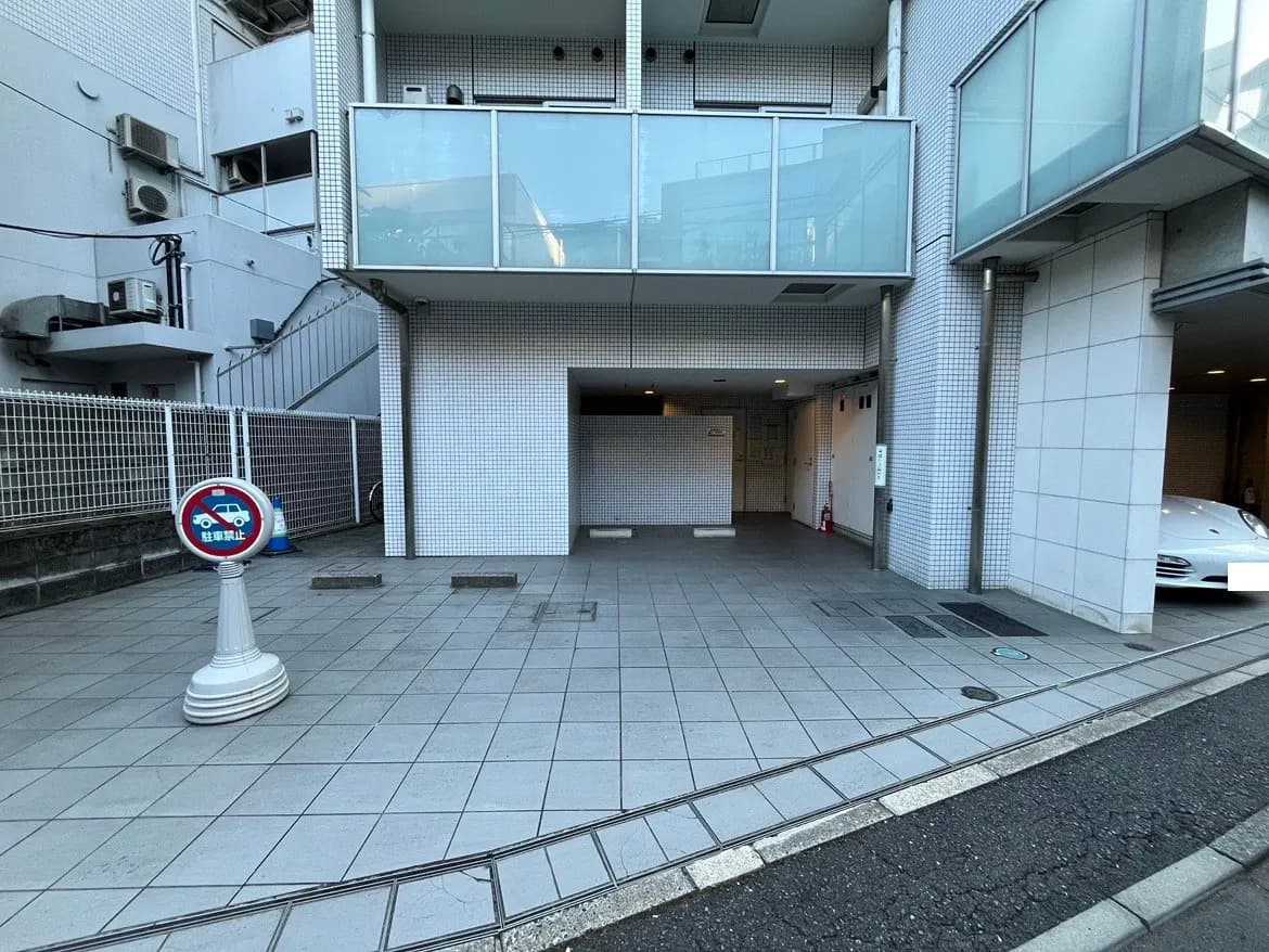 - モダンな外観のビルエントランス、駐車禁止の看板、タイル張りの舗装と自転車置き場がある街角の風景