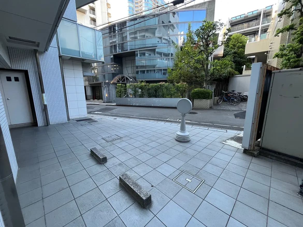 - 都心のアパート前の歩道、周囲に現代的なビルと緑豊かな植栽、舗装されたタイルが特徴の風景