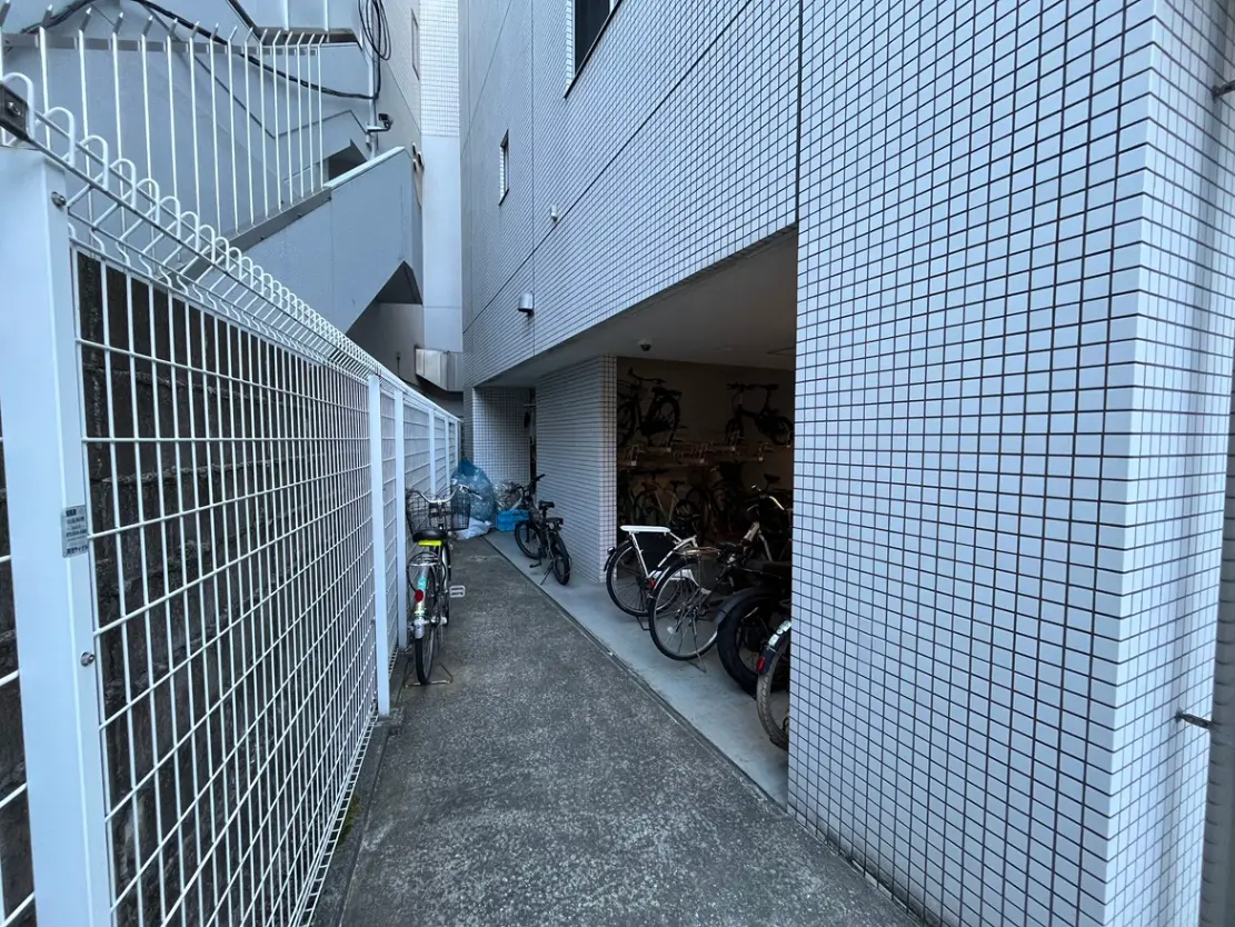 - 自転車が並ぶ建物の横の通路、タイル張りの壁とフェンスに囲まれた静かなスペース