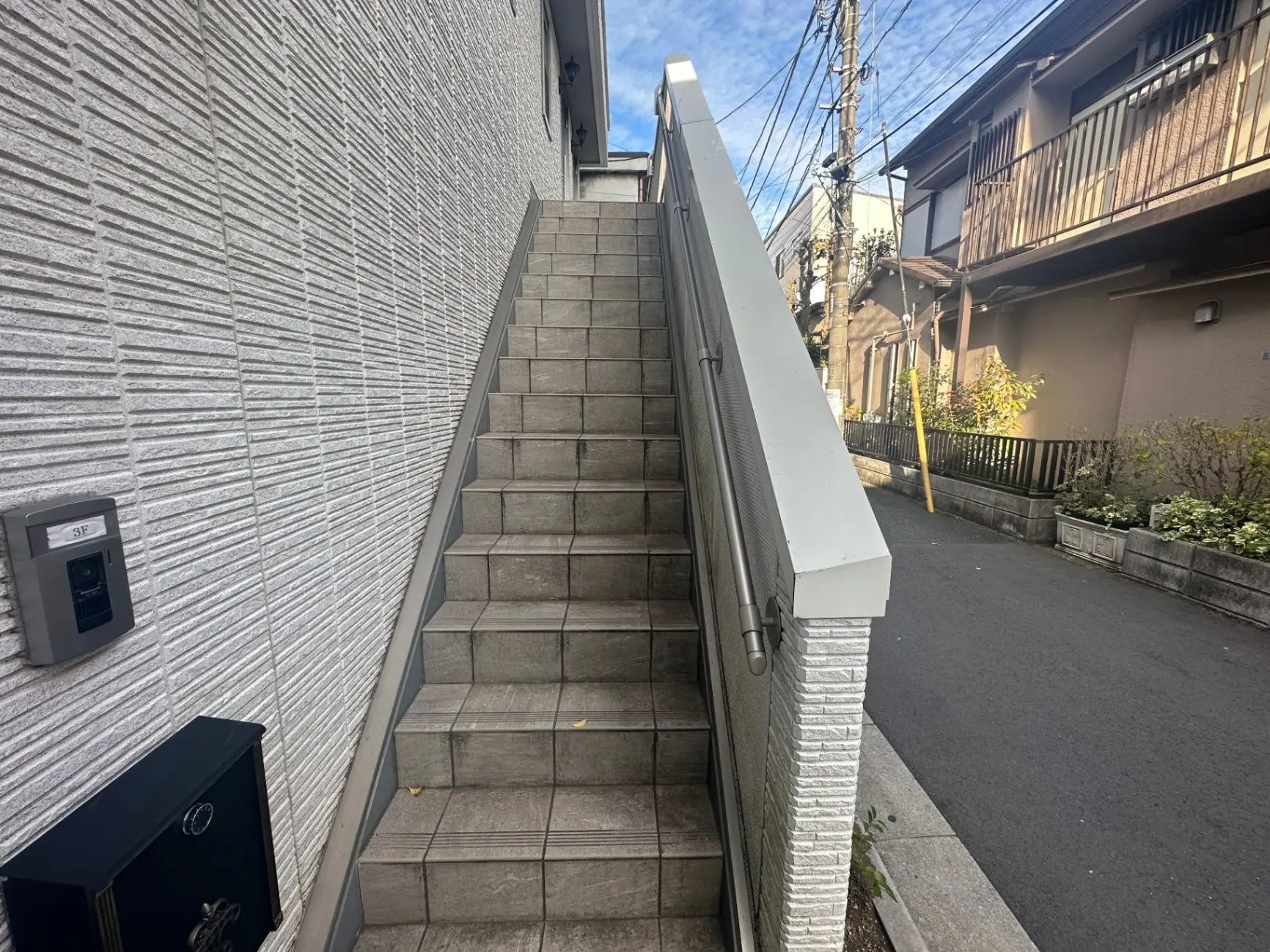 住宅街にある階段と白壁の建物、インターホン付きの入口通路