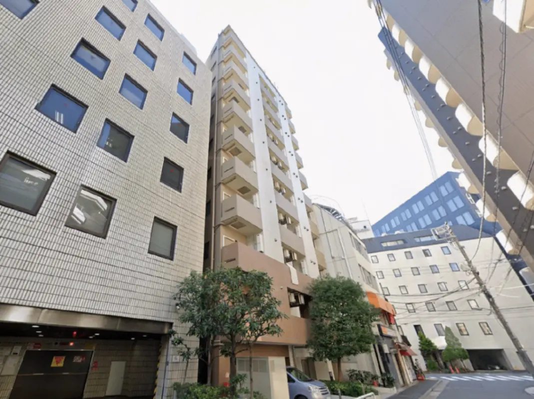 - 都心の高層ビルに囲まれた新しいアパートメントビル、周囲には緑豊かな植栽と駐車スペースが見えるストリートシーン