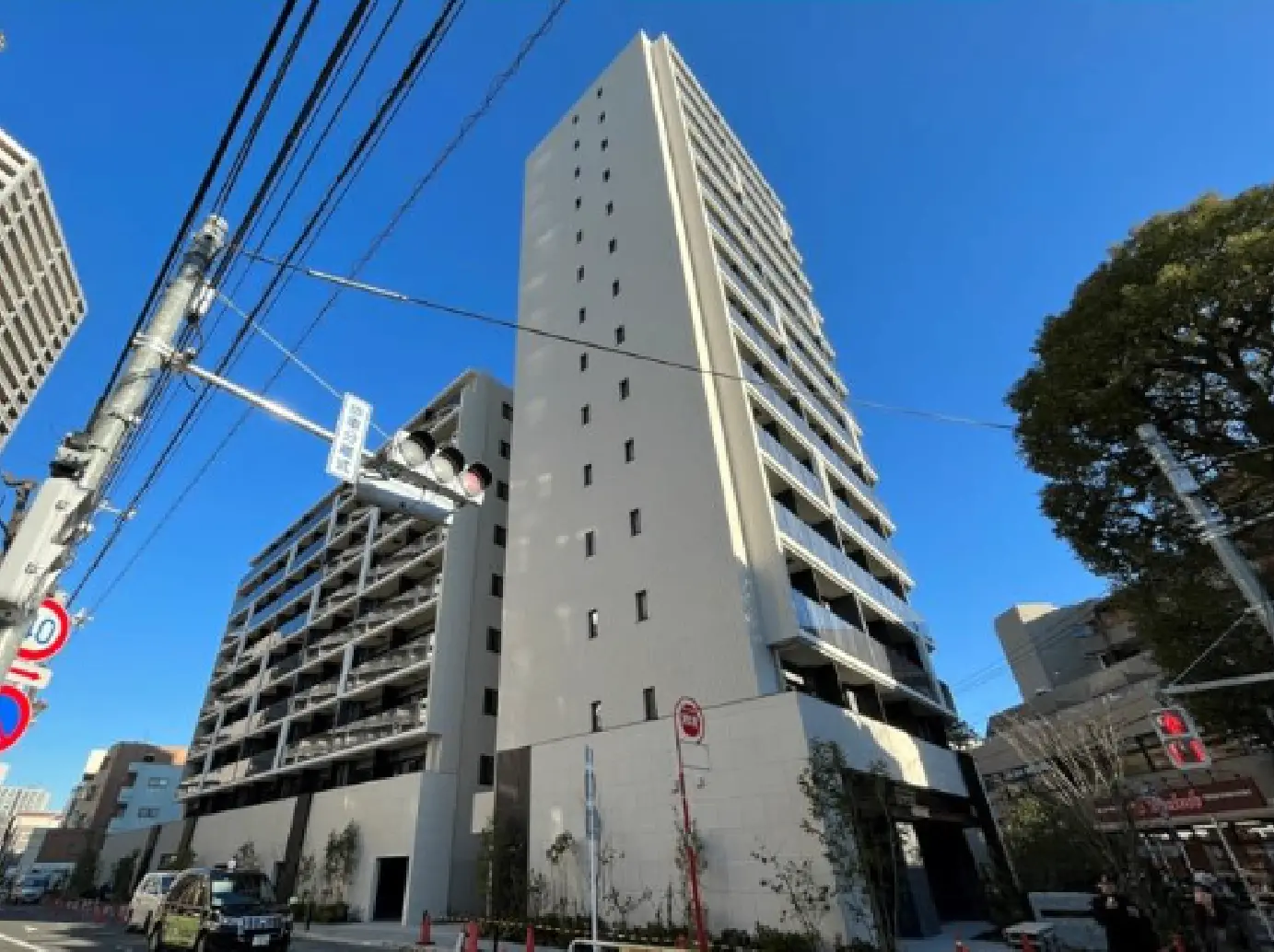 - モダンな高層マンションの外観、青空を背景にしたスタイリッシュなデザイン、周囲の建物と交通信号が映る街並み