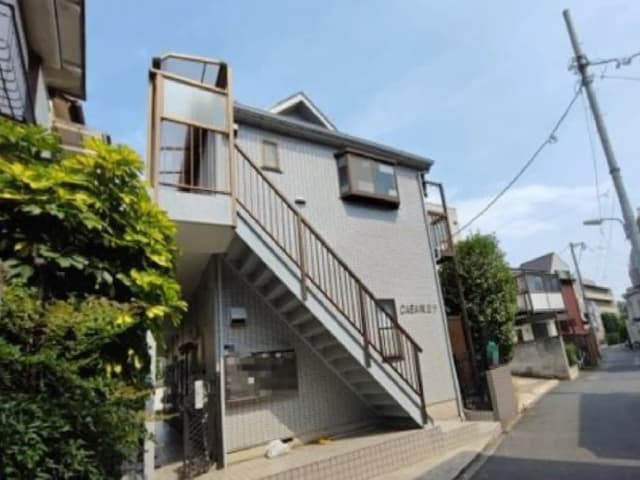 - 自宅の外観、階段付きの2階建て住宅、周囲には自然の緑と静かな通りが広がる景観