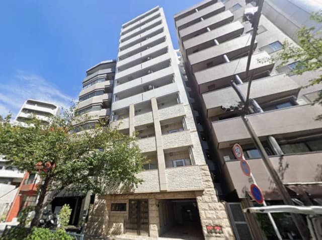 - 現代的なマンションの外観、青空を背景に立つ高層ビル、周囲には緑の木々と交通標識が見える景観