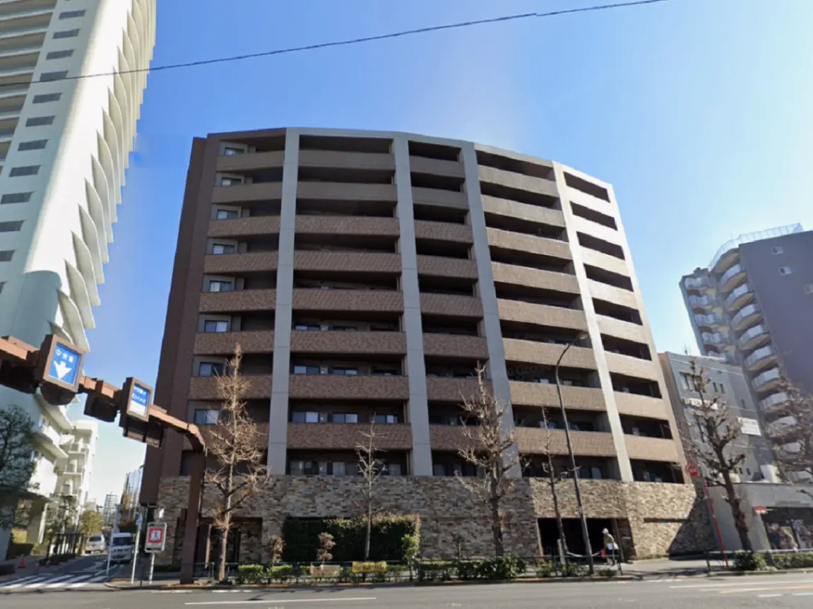 - モダンなデザインのマンション外観、曲線的な形状と明るい空、周囲の街並みが写った画像