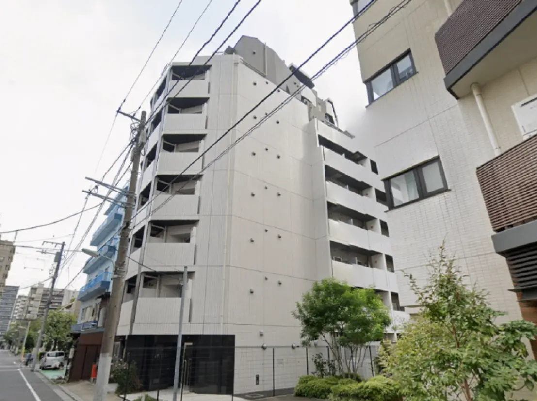 - 都市部にあるモダンなマンションの外観、階段状のバルコニー、周囲の緑と電線が見えるイメージ