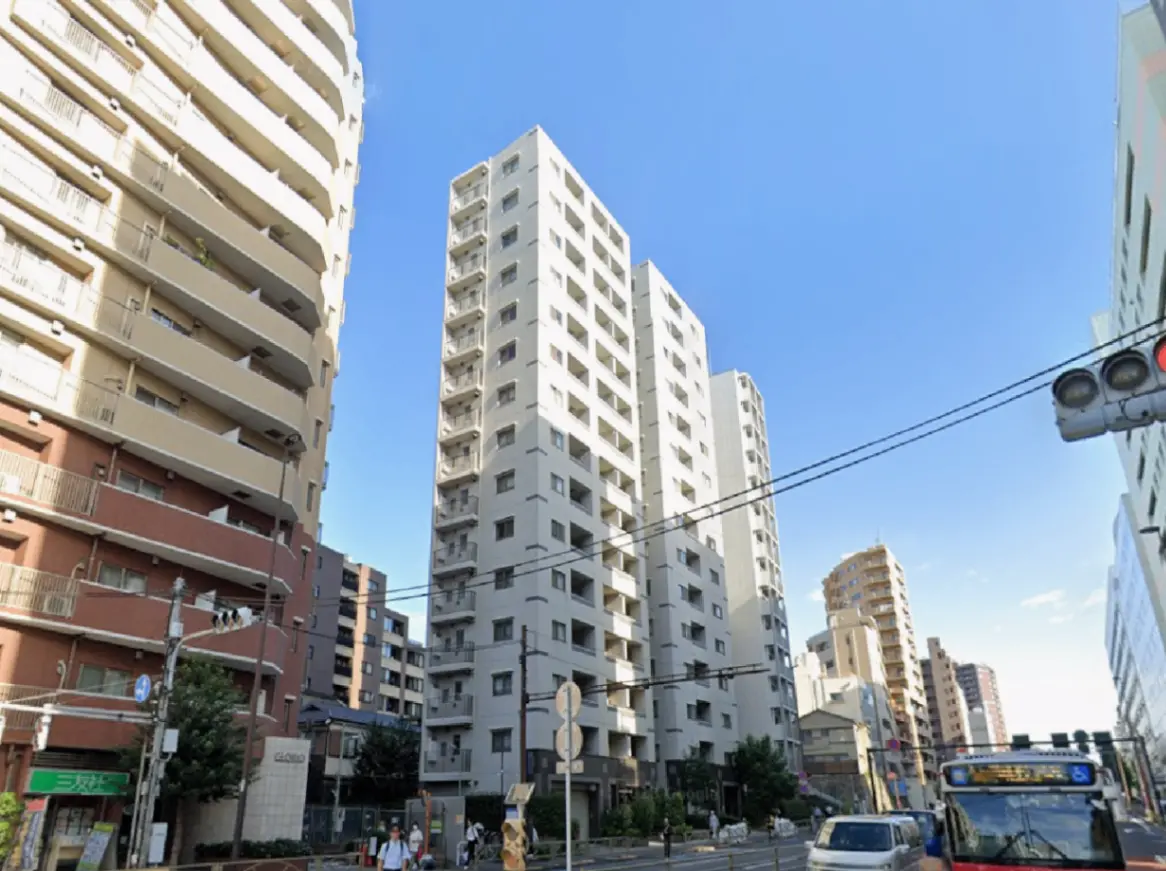 - 都市部に立つ高層マンション、周辺には低層住宅や交通信号、青空が広がる街並みの風景