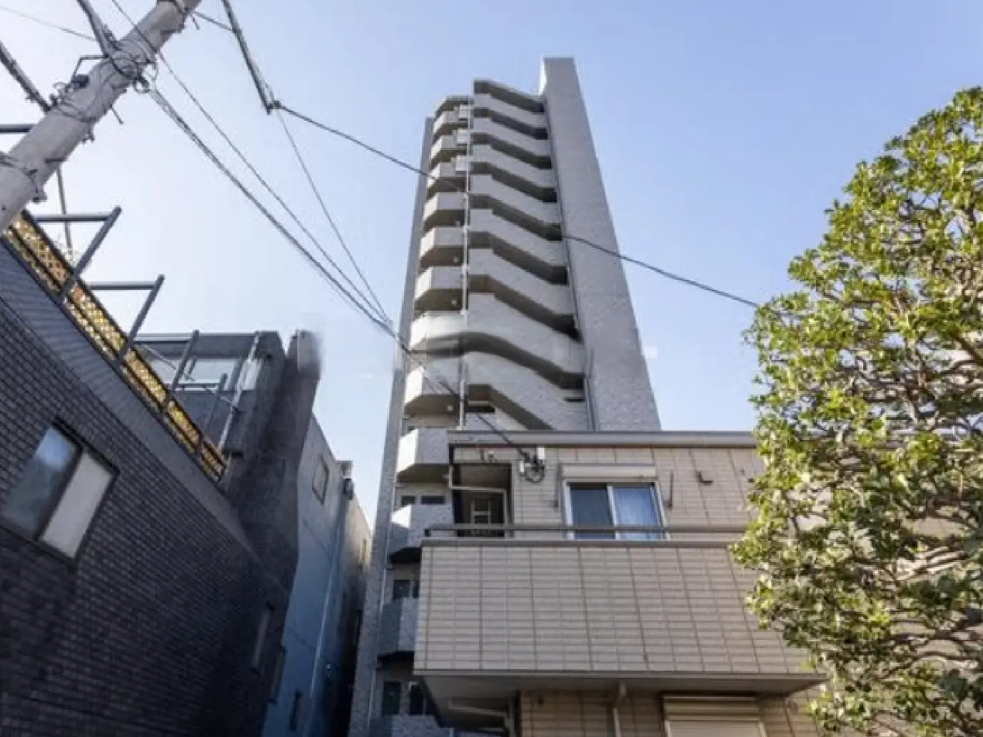 - 高層マンションの外観、白いタイル張り、周囲の建物と青空が広がる風景