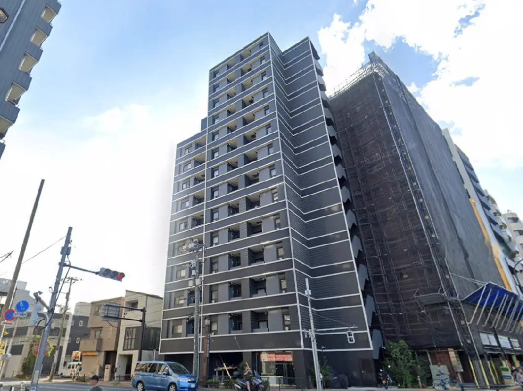 - シンプルでモダンなデザインのマンション、外観は黒と白のストライプ、周囲に商業施設と交通信号が見える市街地の風景