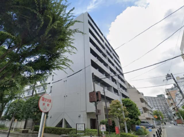 - 近代的なマンションの外観、周囲に緑がある街並みと青空の下に立つ建物