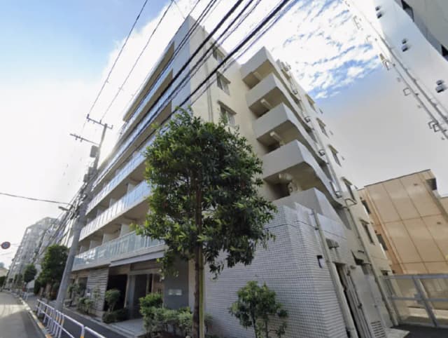 - モダンなデザインのマンション外観、青空と電線が写る都市風景、緑の植栽が周囲を彩る