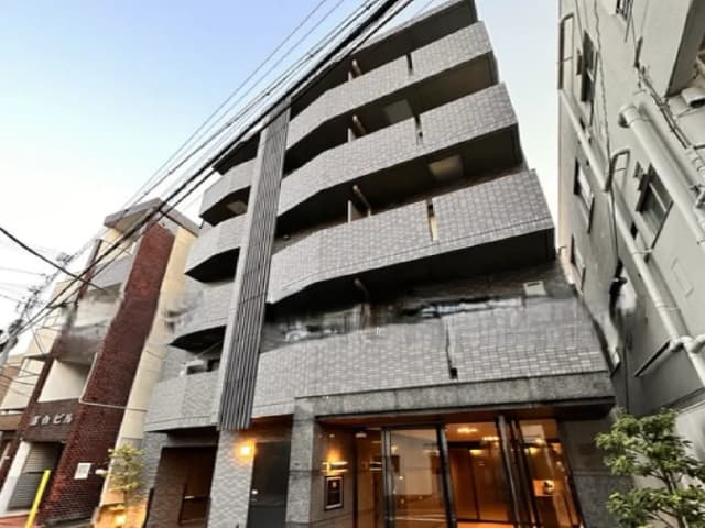 - 現代的なデザインのマンション外観、グレーのタイルとバルコニーが特徴、本エントランスには明るい照明と植栽が配置された景観