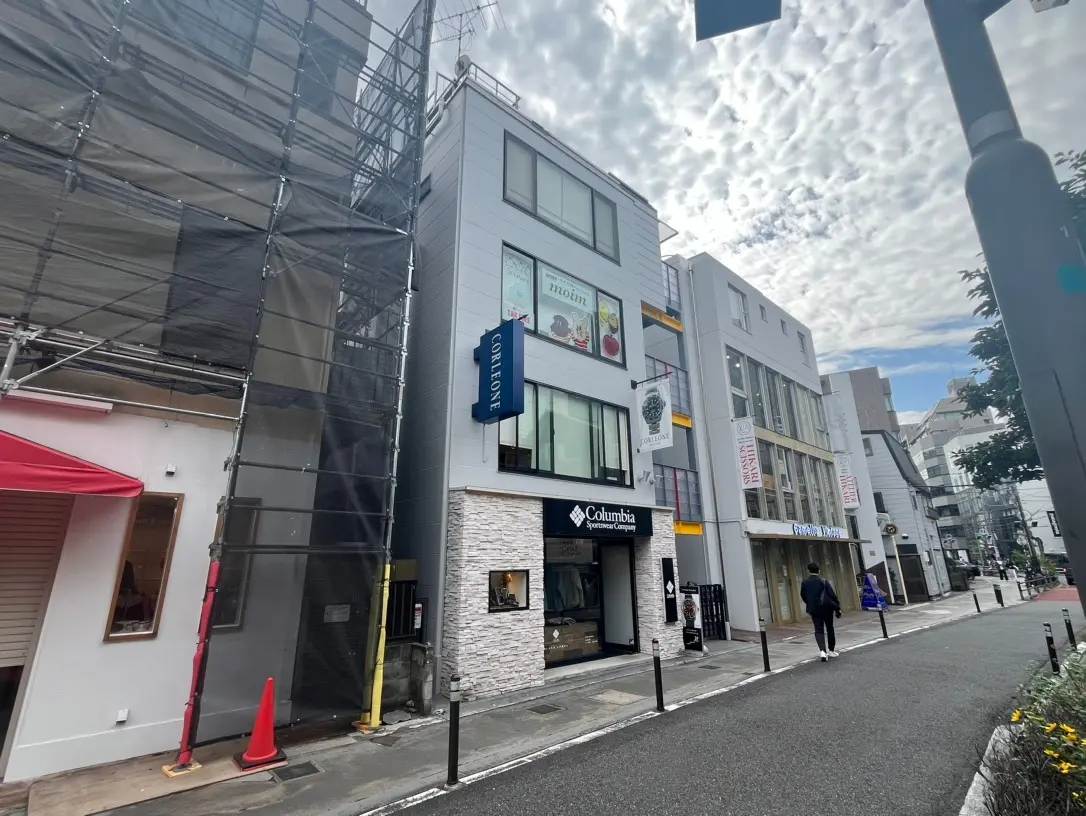 工事中のビルと店舗が並ぶ市街地の通り、雲模様の空と歩行者