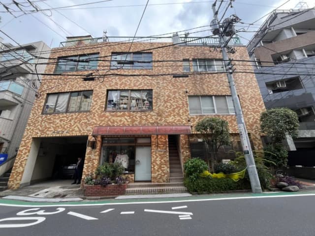 都市の路面に面したレンガ造りのビル、一階には小さな店舗があり駐車スペースつき